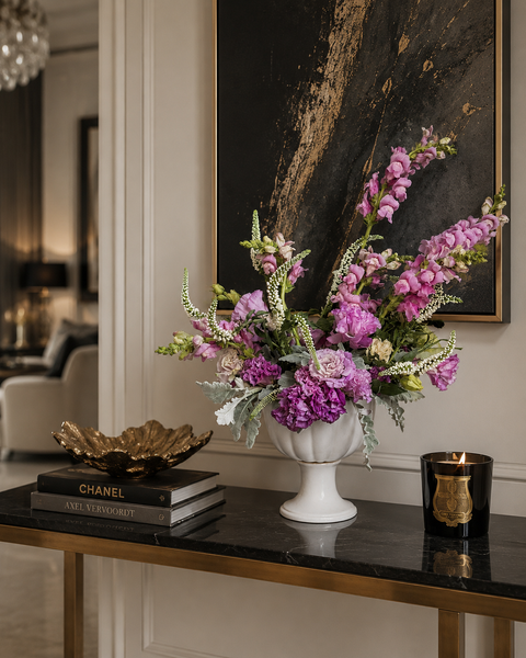 Puple Floral arrangement in a white vase on a dark marble table with books and a candle.
