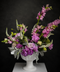 Luxury purple floral arrangement with snapdragons and lisianthus in a white ceramic pedestal vase against a dark background