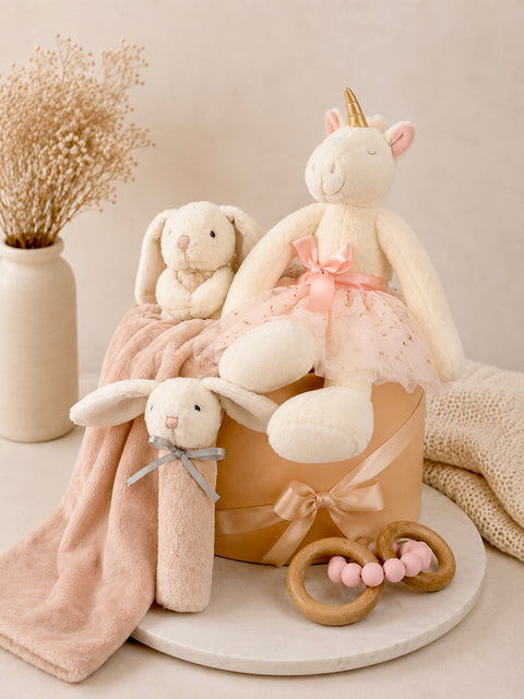 Children's toys including a plush unicorn and bunnies on a neutral background