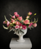 Luxury pink rose arrangement with lisianthus and silvery foliage in a white ceramic pedestal vase against a dark background