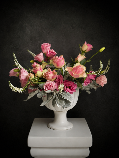 Luxury pink rose arrangement with lisianthus and silvery foliage in a white ceramic pedestal vase against a dark background