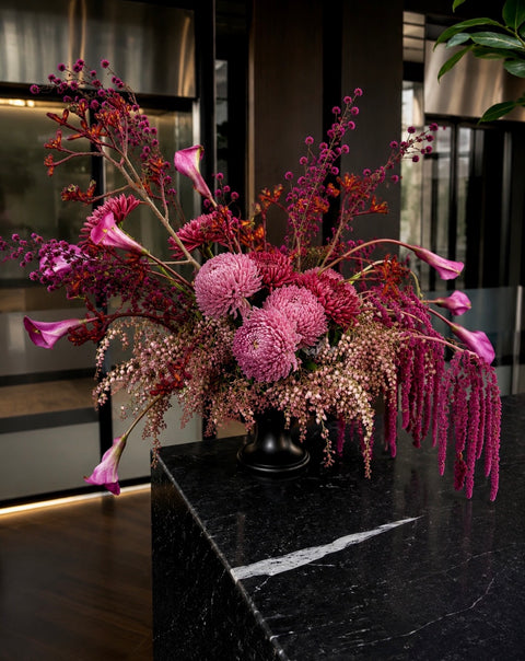 Burgundy and deep dusty pink floral arrangement in black compote vase featuring burgundy calla lilies, chrysanthemums, amaranthys and kangaroo paw