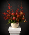 Decorative floral arrangement with red orchids and Natives in a beige vase on a white pedestal against a dark background