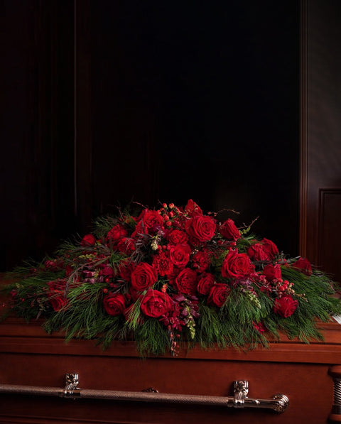 Red floral arrangement on a wooden casket against a dark background