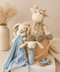 Children's toys including a plush giraffe, bunny, and baby comfort blanket in a bucket on a light surface.