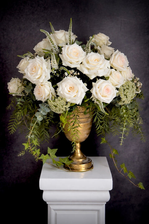 Floral arrangement with white roses and greenery in a gold urn 