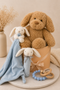 Stuffed baby toys hamper including a teddy bear, bunny, and blue comfort blanket on a beige surface.