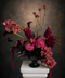 Moody Burgunduy Floral arrangement in a black vase on a white pedestal against a dark background with Cybidium orchids, snapdragons, amaranthys and Allums