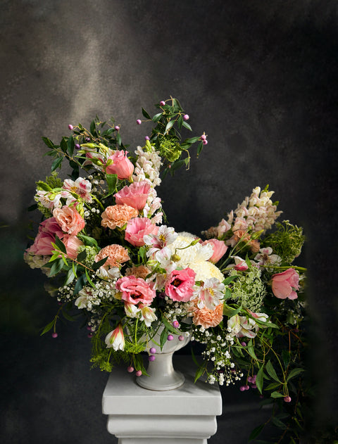Luxurious Garden Floral arrangement in a white vase on a dark background featuring Pink Lisianthus and peach carnations