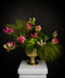 Luxury sculptural floral arrangement with pink gloriosa lilies, green chrysanthemums, and flowing foliage in a gold pedestal vase against a dark background