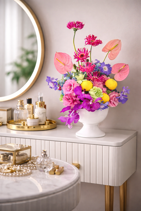 Colourful and bright floral arrangement in a white vase on a marble surface with decorative items.