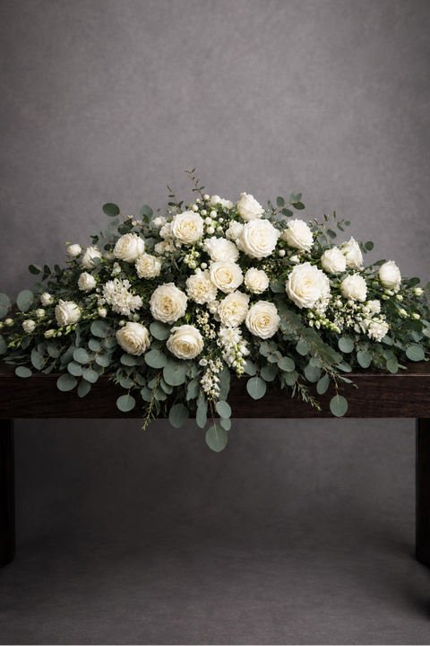 White flower casket cover for funeral with roses, carnations, orchids, eucalyptus and snapdragons